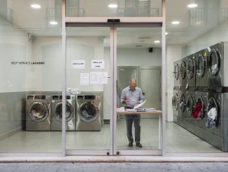 Titolare di una lavanderia self-service controlla una bozza pubblicitaria davanti alla vetrina del negozio